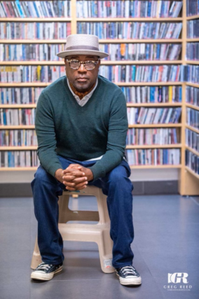 Michael Valentine sitting in WDNA studio, surrounded by a vast collection of jazz CDs at the WDNA Music Library.