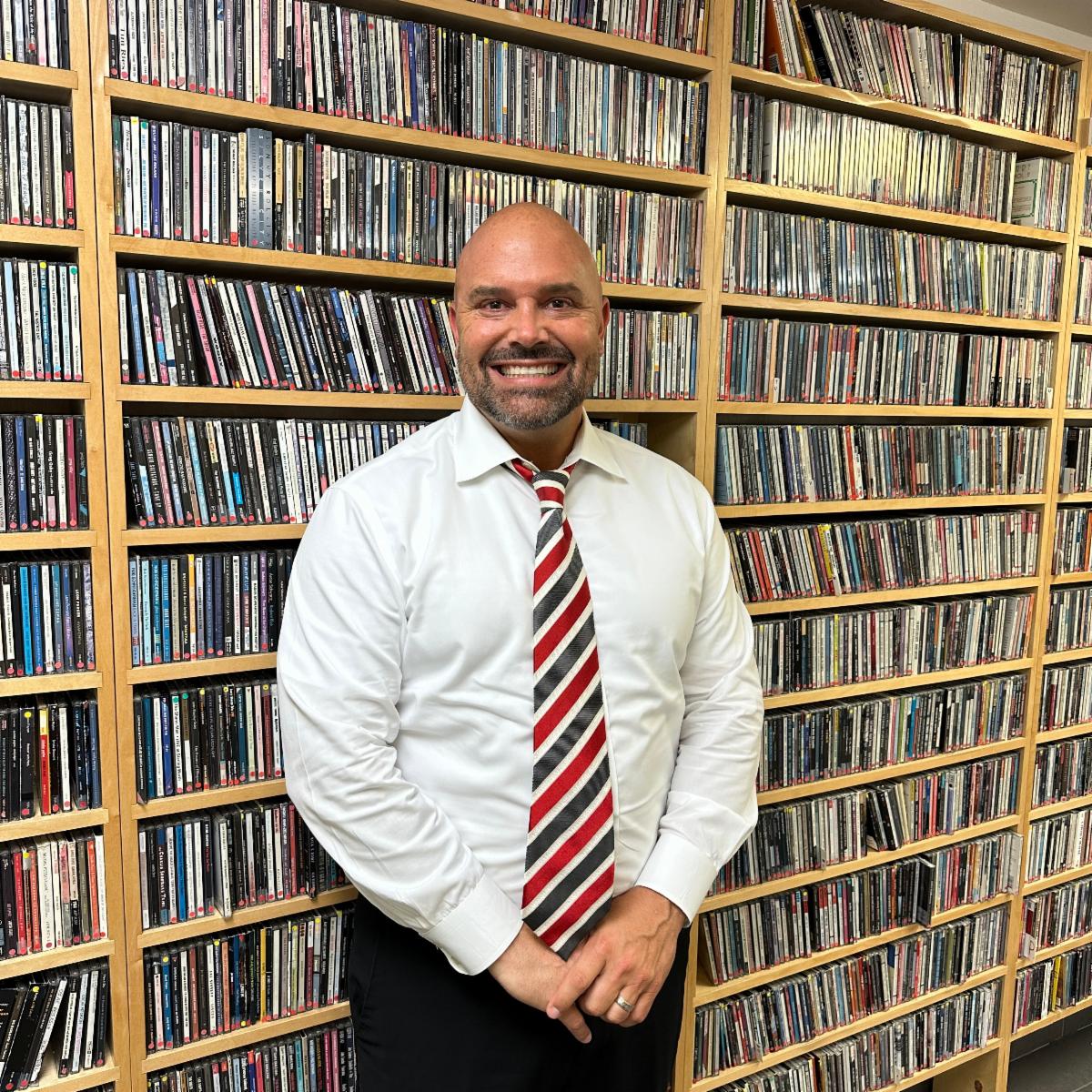 Brandon Buth, Assistant General Manager of WDNA 88.9FM, standing in front of a wall of CDs in WDNA's Music Library, contributing to the station’s jazz and Latin jazz programming.