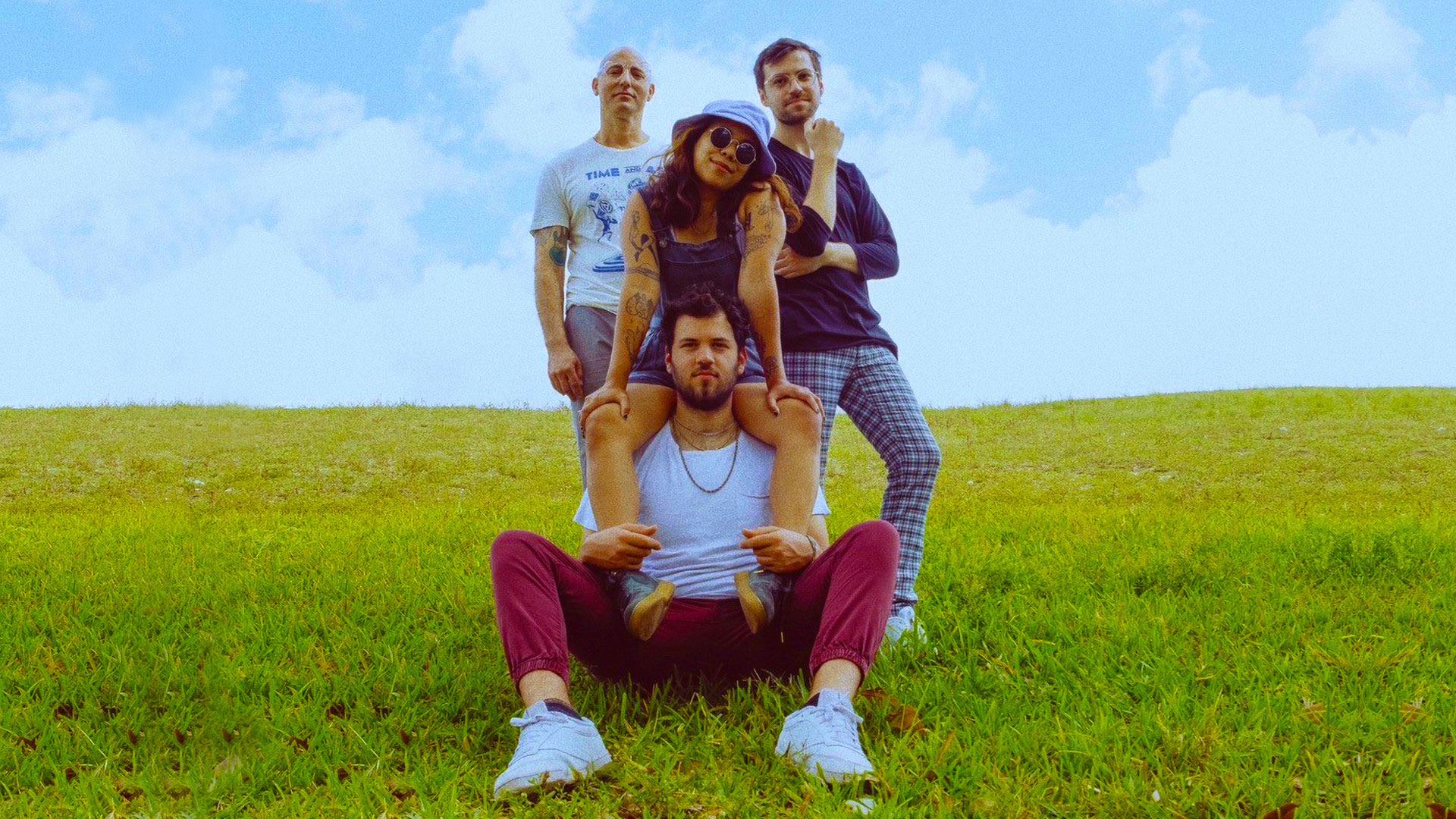 Abstract Citizen band members posing outdoors, with vibrant greenery and a bright blue sky background, promoting their live performance at the Adrienne Arsht Center.